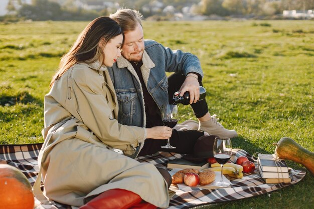 Pareja romántica en ropa de moda sentado en la naturaleza sobre una alfombra de picnic. Hombre vestido con chaqueta y abrigo de mujer