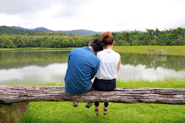 Foto gratuita pareja romántica sentada en la madera y disfrutando de la vista de un lago tranquilo