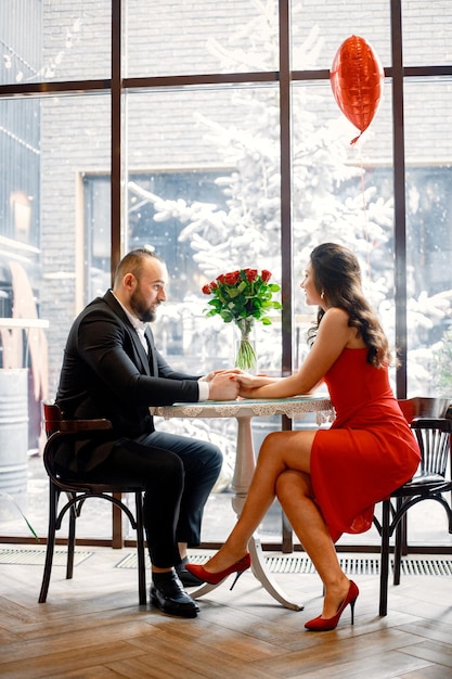 Pareja romántica sentada en un restaurante en una cita cerca de una ventana grande