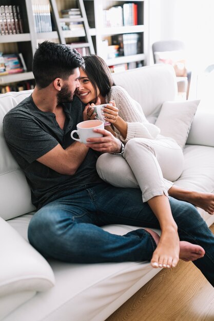 Pareja romántica sentado en el sofá con taza de café mirando el uno al otro