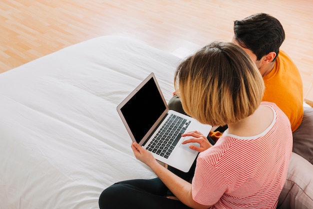 Pareja sin rostro usando la computadora portátil en la cama