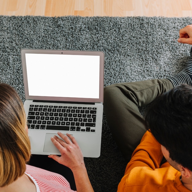 Pareja sin rostro usando la computadora portátil en el piso