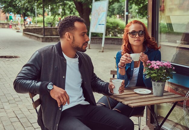 Una pareja saliendo tomando café, sentada cerca de la cafetería. Al aire libre en una cita.