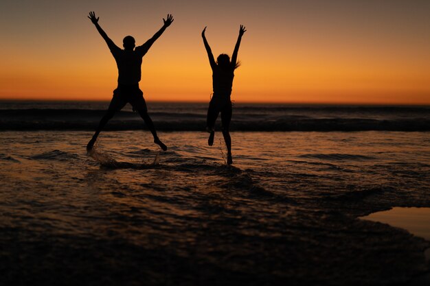 Pareja saltando juntos con los brazos en la playa