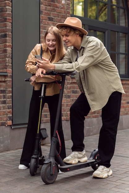 Foto gratuita pareja con scooters eléctricos y smartphone en la ciudad.