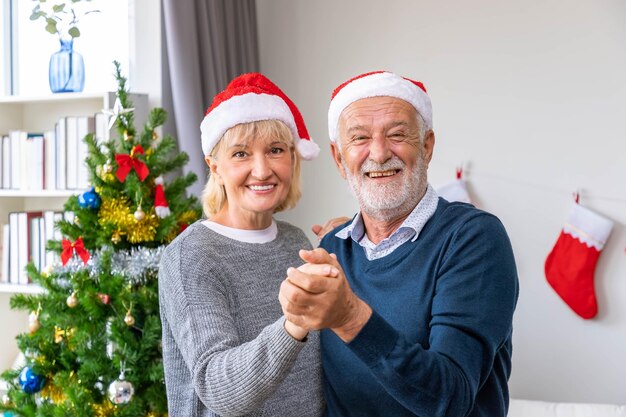 Pareja senior caucásica anciano y mujer bailando juntos en la sala de estar con árbol de Navidad en segundo plano.