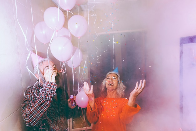 Pareja senior celebrando a la pareja en la habitación llena de humo decorada con globos rosados