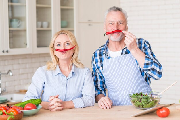 Pareja senior con chiles rojos en sus labios superiores mirando a cámara