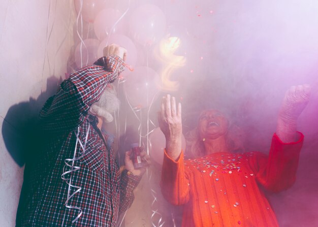 Pareja senior disfrutando de la fiesta de cumpleaños en la sala llena de humo