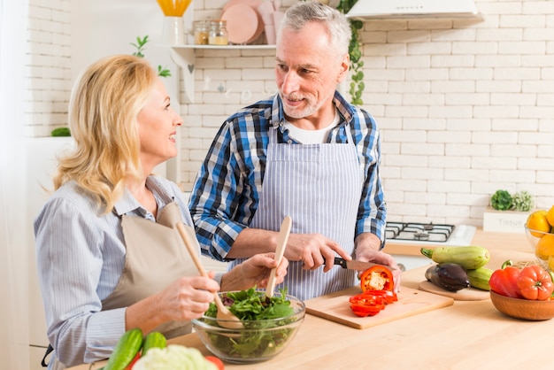 Foto gratuita pareja senior preparando la ensalada en la cocina moderna mirando el uno al otro