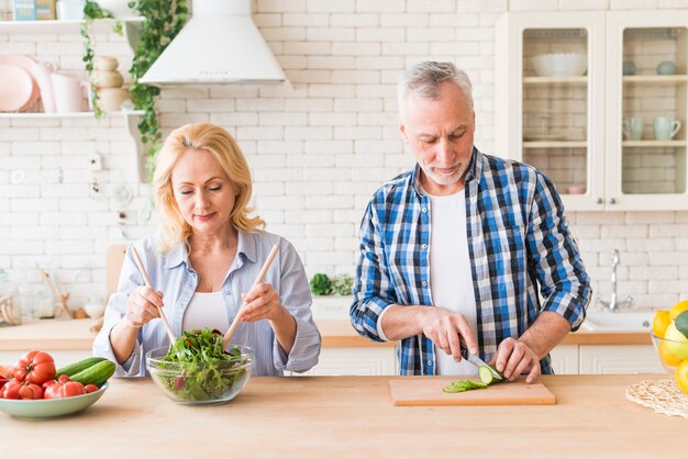 Pareja senior preparando la ensalada en la cocina moderna