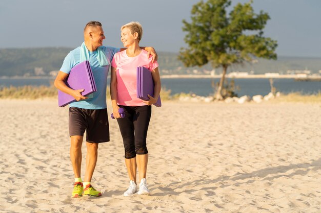 Pareja senior sonriente con equipo de trabajo en la playa y espacio de copia