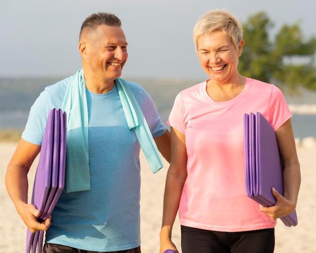 Foto gratuita pareja senior sonriente con equipo de trabajo en la playa