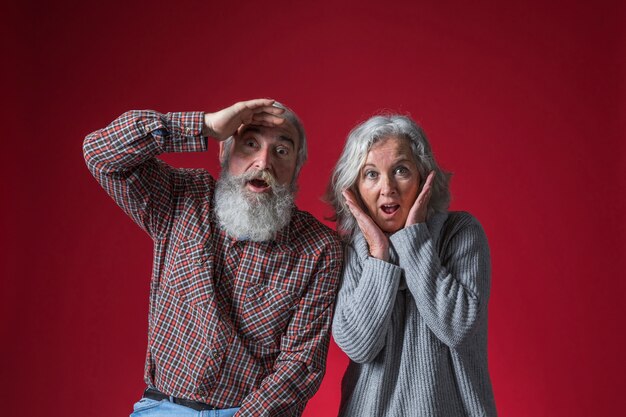 Pareja senior sorprendido mirando a la cámara contra el fondo rojo