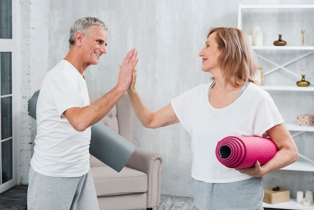 Pareja senior sosteniendo esteras de yoga dando cinco alta