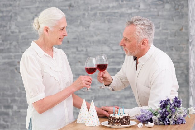 Pareja Senior tintineo copa de vino en la fiesta de cumpleaños