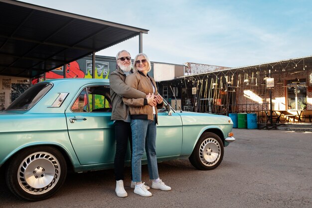 Pareja senior de tiro completo de pie cerca del coche