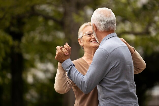 Pareja senior de tiro medio bailando en la naturaleza