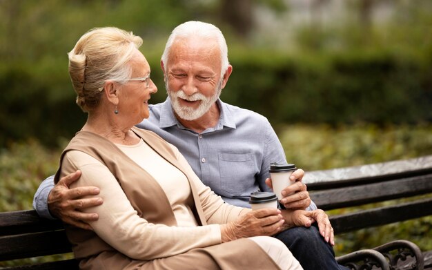 Pareja senior de tiro medio en un banco con tazas