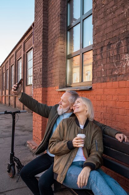 Pareja senior de tiro medio tomando selfie en un banco