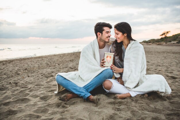 Pareja sentada en la arena con una vela y una manta