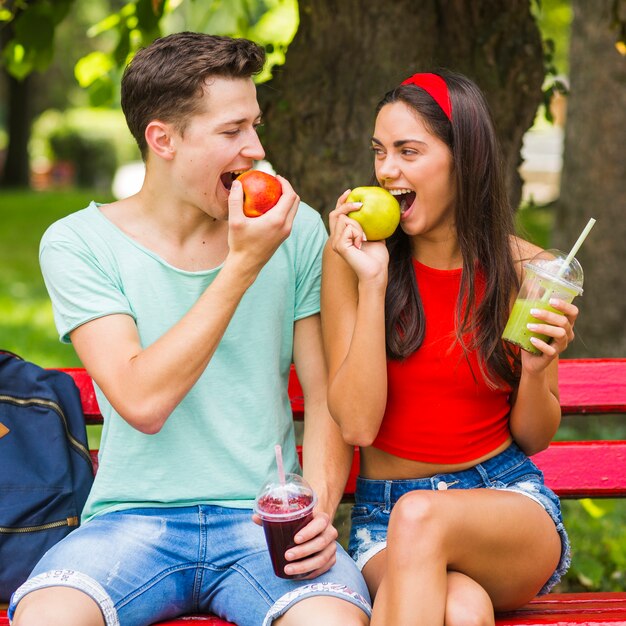 Pareja sentada en el banco comiendo manzanas maduras con batidos