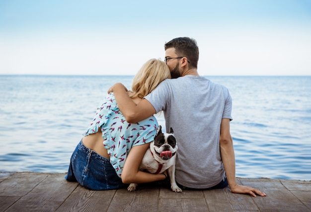 Pareja sentada con bulldog francés cerca del mar