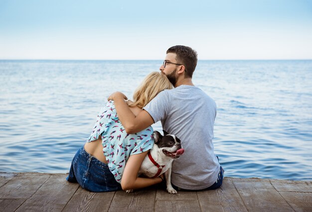 Pareja sentada con bulldog francés cerca del mar