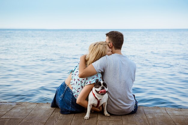 Pareja sentada con bulldog francés cerca del mar