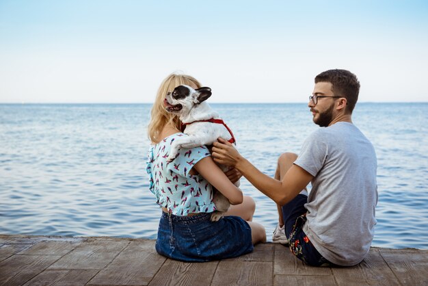 Pareja sentada con bulldog francés cerca del mar