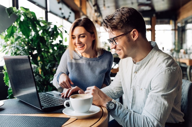 Una pareja sentada en el café riéndose alegremente, mirando la pantalla del portátil