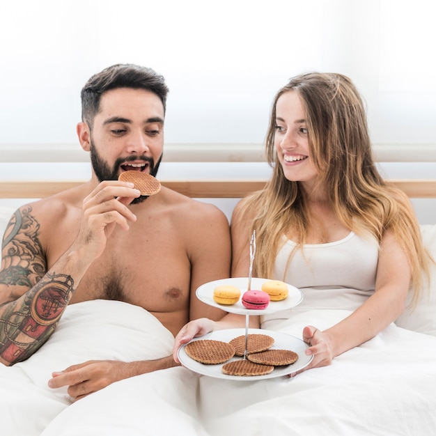 Foto gratuita pareja sentada en la cama desayunando por la mañana