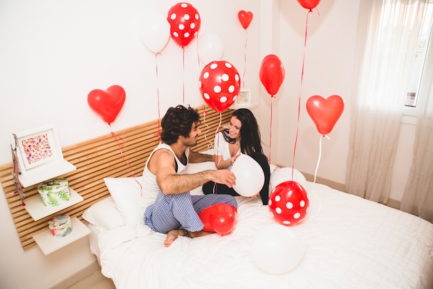 Pareja sentada en una cama con globos por todas partes