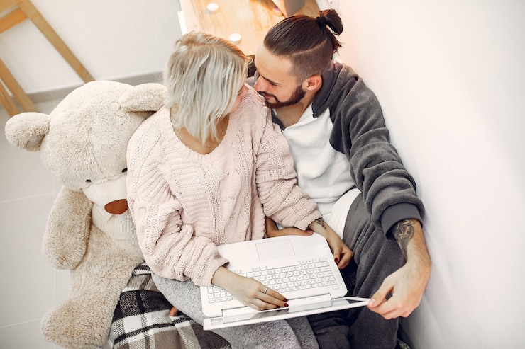 Foto gratuito pareja sentada en una cama en una habitación y usa una computadora portátil