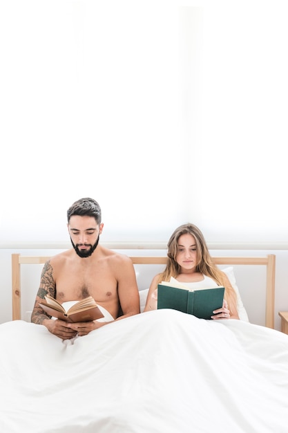 Pareja sentada en la cama leyendo el libro