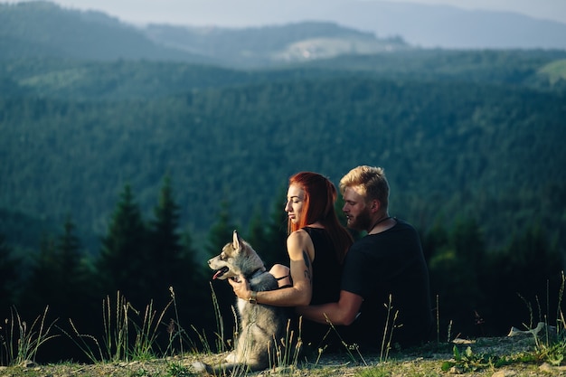 Pareja sentada en un campo verde mirando la naturaleza con su perro