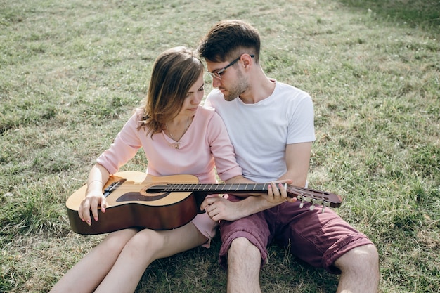 Foto gratuita pareja sentada en el césped con una guitarra