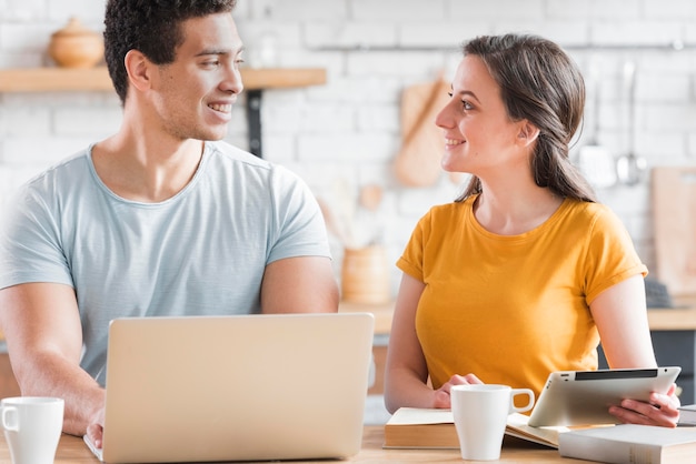 Pareja sentada en la cocina con laptop y tablet