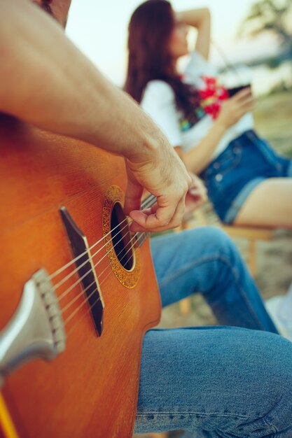 Pareja sentada y descansando en la playa tocando la guitarra en un día de verano cerca del río