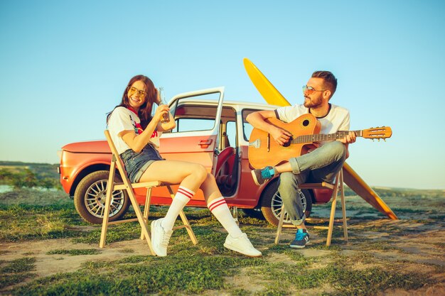 Pareja sentada y descansando en la playa tocando la guitarra en un día de verano cerca del río