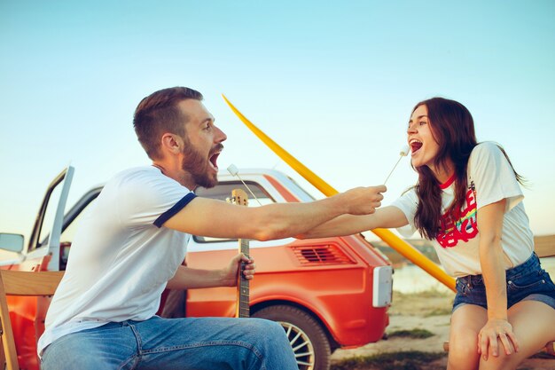 Pareja sentada y descansando en la playa tocando la guitarra en un día de verano cerca del río