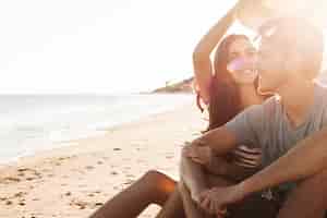 Foto gratuita pareja sentada a lado del mar con el sol brillando