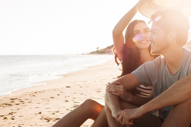 Pareja sentada a lado del mar con el sol brillando