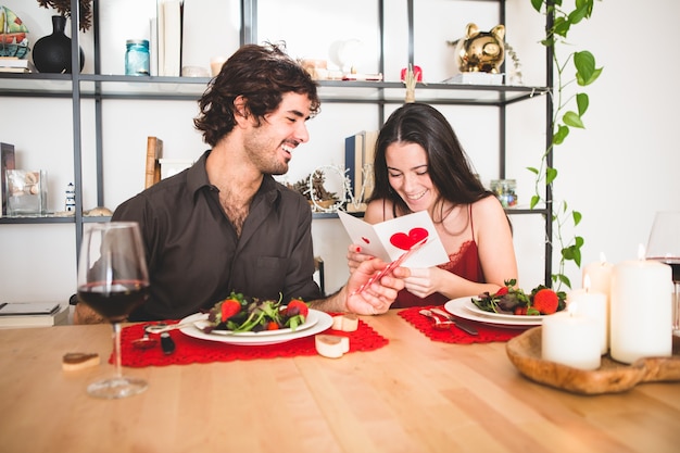 Pareja sentada en una mesa para comer mientras ella lee una postal romántica