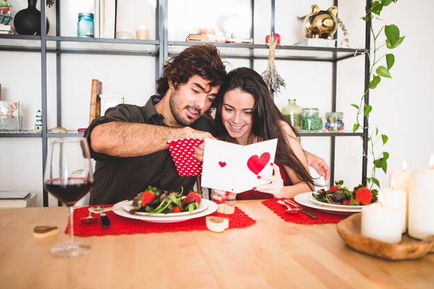 Pareja sentada en una mesa para comer mientras ella lee una postal romántica