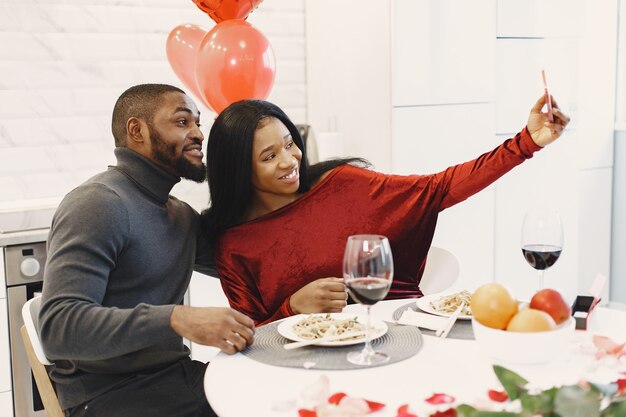 Pareja sentada a la mesa, comer, tomar fotos y reír en el día de San Valentín