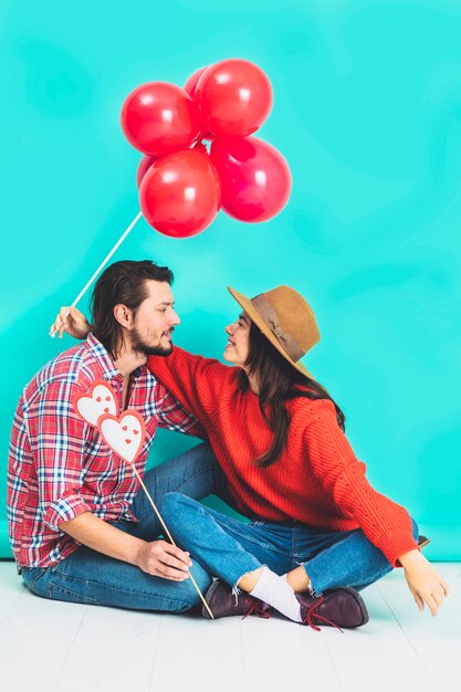 Pareja sentada en el piso con globos rojos y corazones en palo