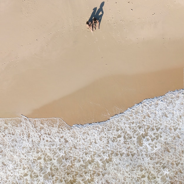 Pareja sentada en la playa cerca de las olas de espuma