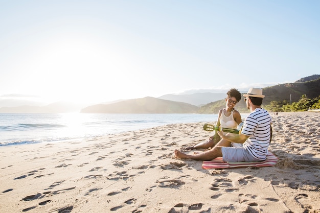 Foto gratuita pareja sentada en la playa con guitarra