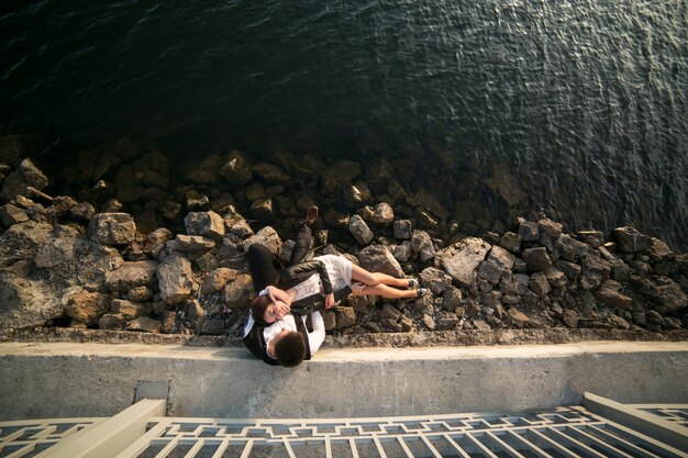 Pareja sentada en las rocas junto al mar visto desde arriba